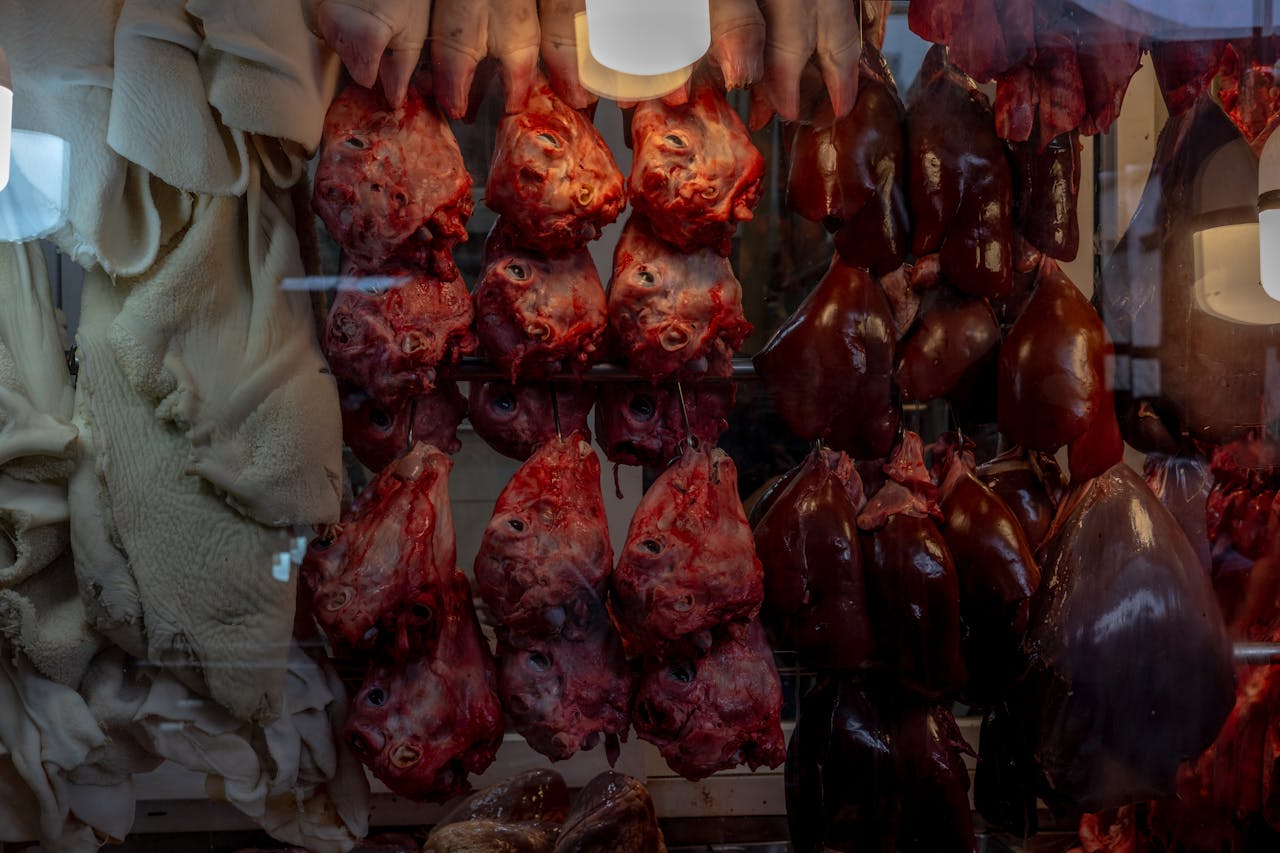 Services Close-up of various meat and organ cuts hanging in a butcher shop display window.