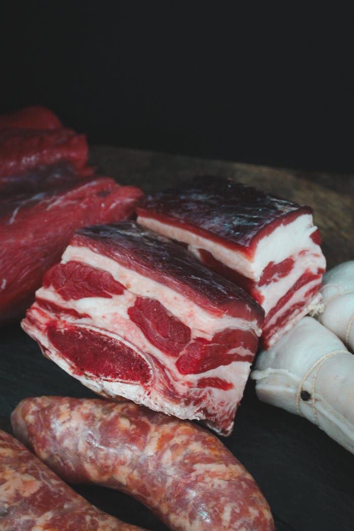 Services A diverse selection of raw meats including ribs and sausages on a dark surface.