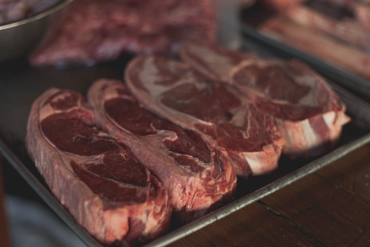 Services High-quality close-up image of raw steaks ready for cooking on a metal tray.